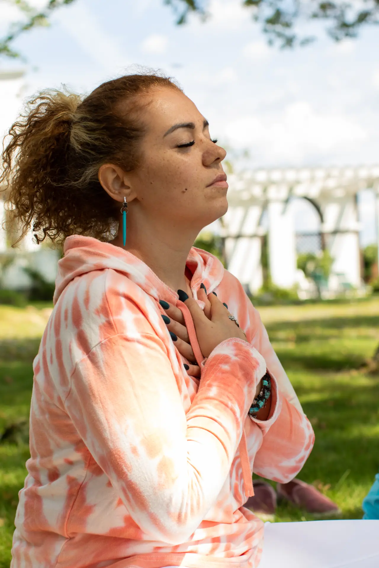 A woman seated outdoors with her hands over her heart