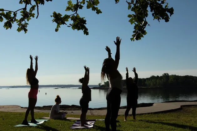 Women raising their arms in yoga by the water at sunset